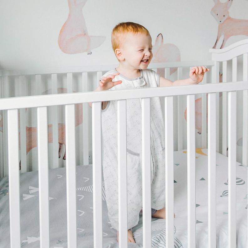 Baby in a crib wearing Tealbee Love Milk Dreamsuit and Toddler Sleep Sack with legs
