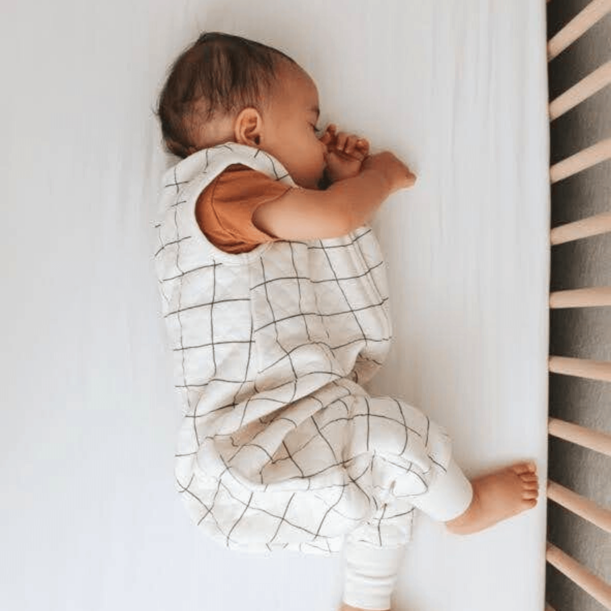 Sleeping baby on a crib wearing Tealbee Deamsuit Checkered
