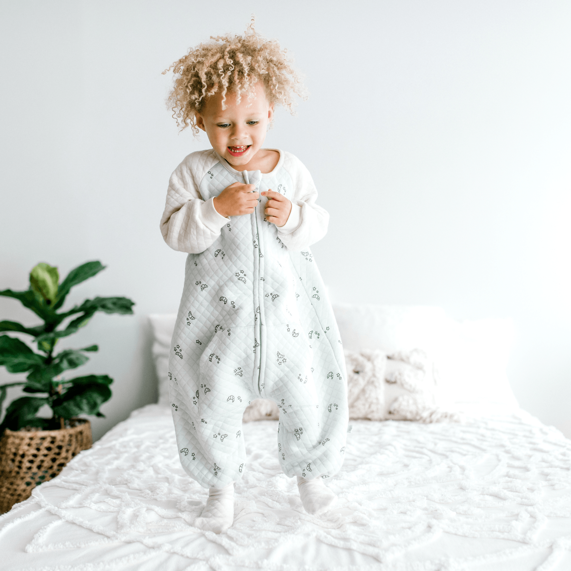 Baby walking on the bed wearing Croissant Dreamsie - 0.8 TOG Sleep Sack With Sleeves - Tealbee