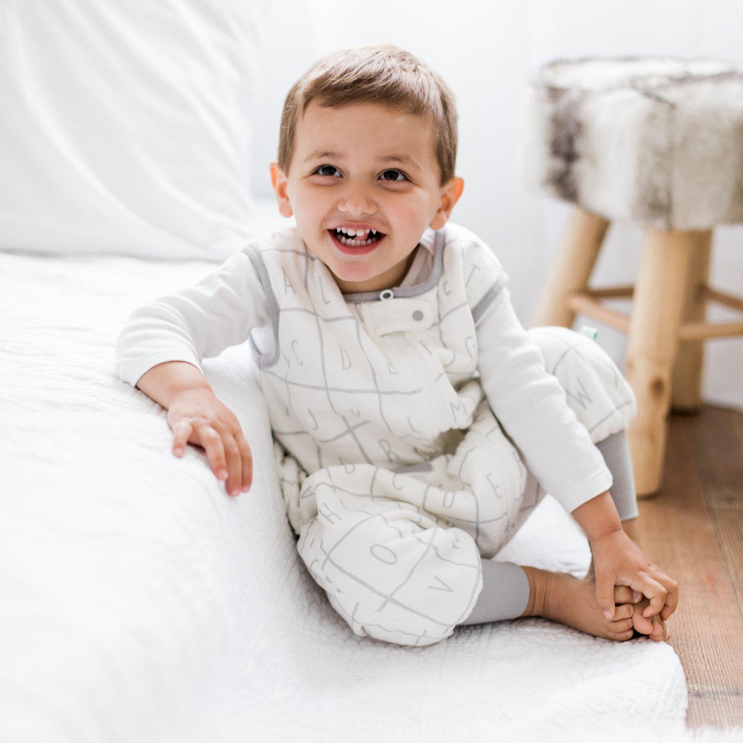 Baby sitting down on a bed wearing Tealbee Dreamsuit Alphabet 1.2 TOG. 