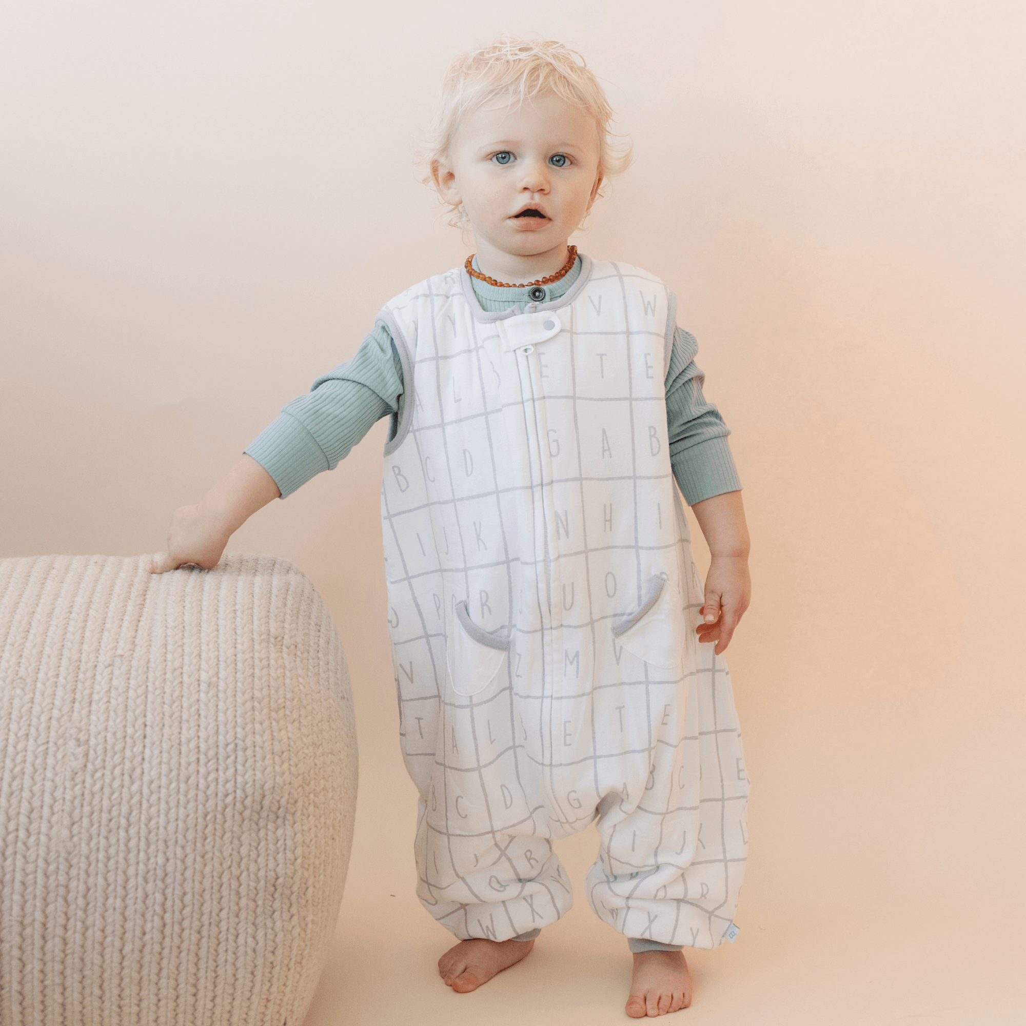 Toddler wearing Tealbee Dreamsuit Alphabet. print front view, alphabet blocks are light grey and each block measures a couple of inches