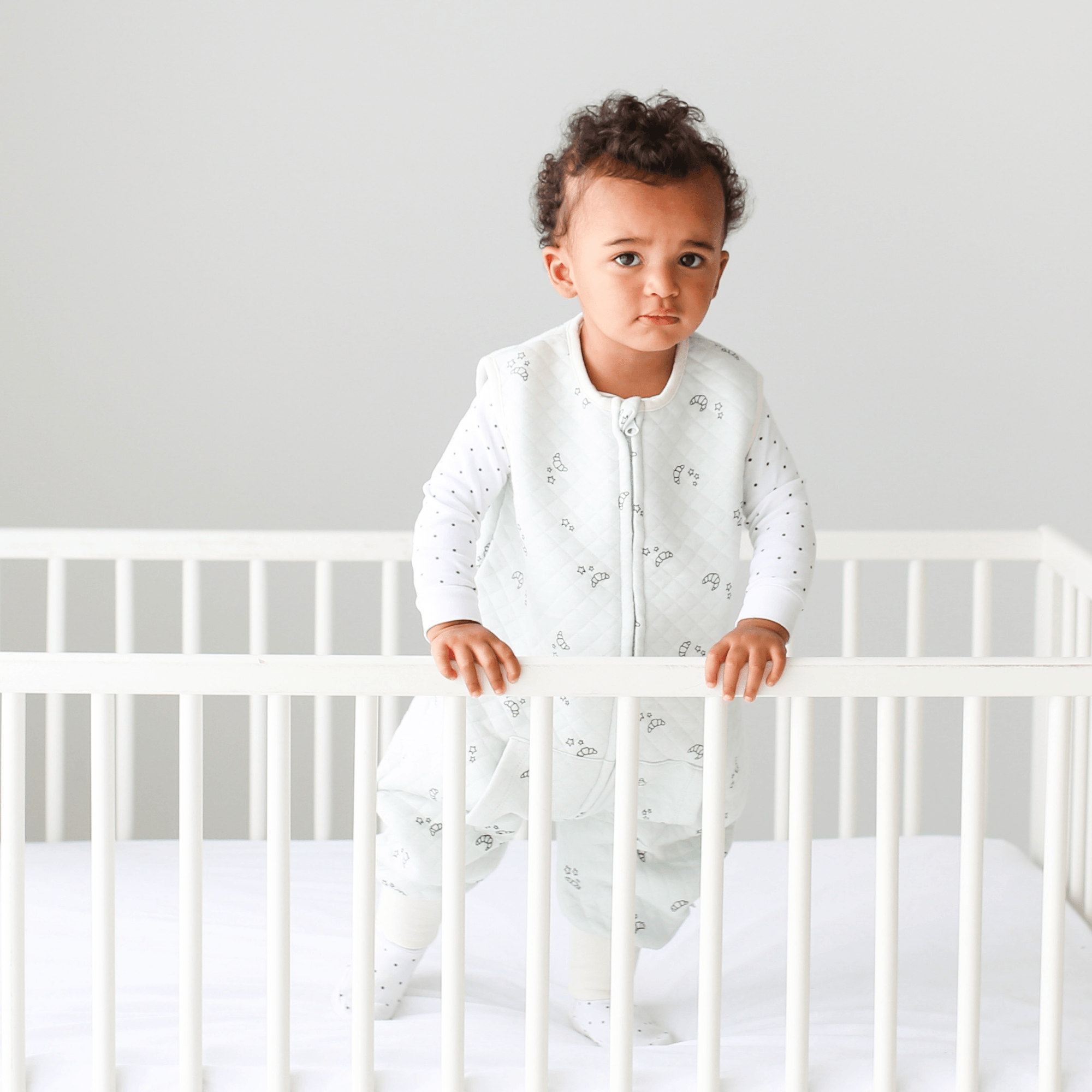 Toddler in a crib wearing Tealbee Croissant Dreamsuit Toddler Sleep Sack